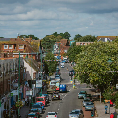 Looking north along Station Road New Milton with shops either side and cars on the road.